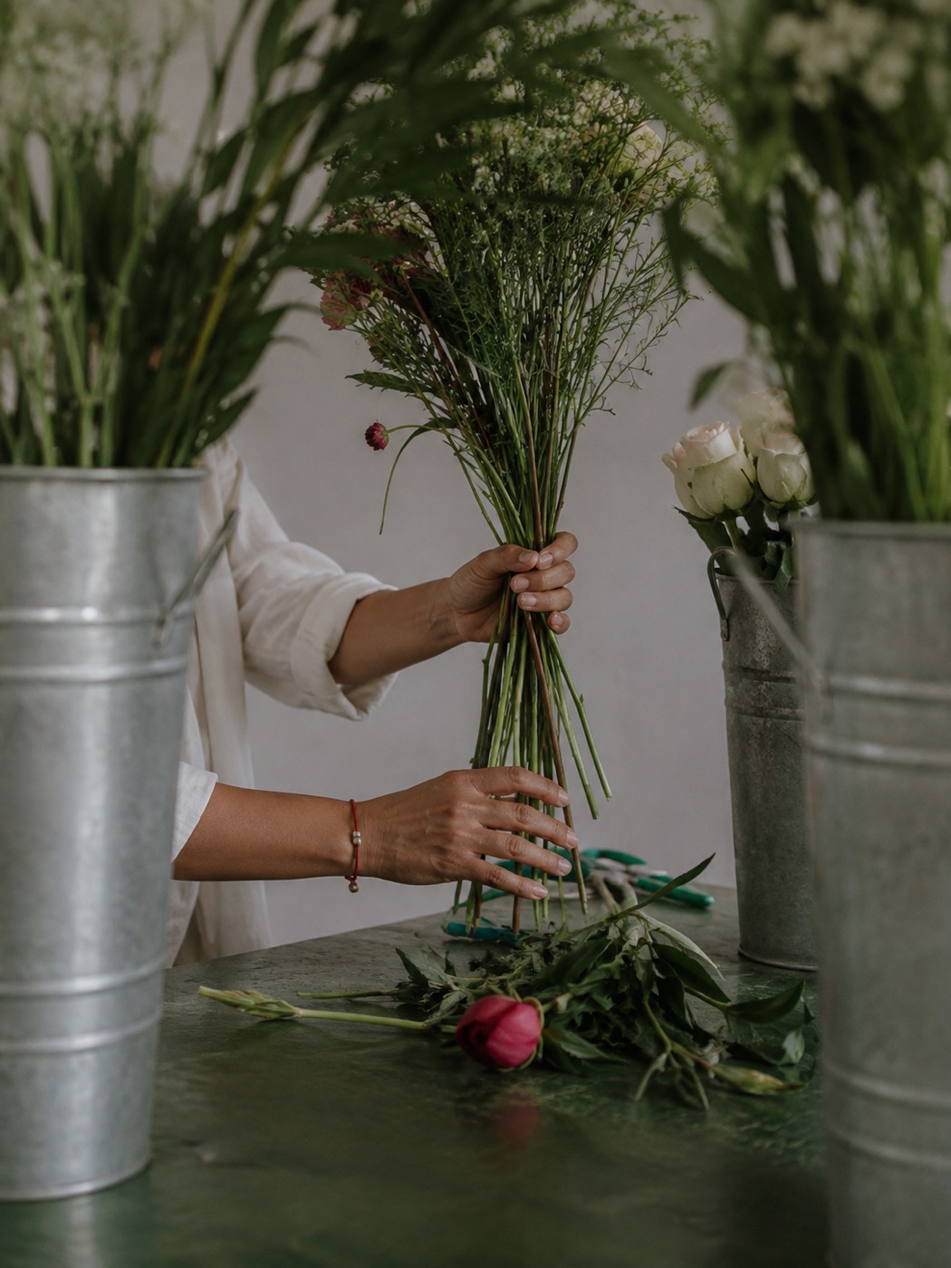 Manos armando un ramo de flores frescas junto a cubetas galvanizadas