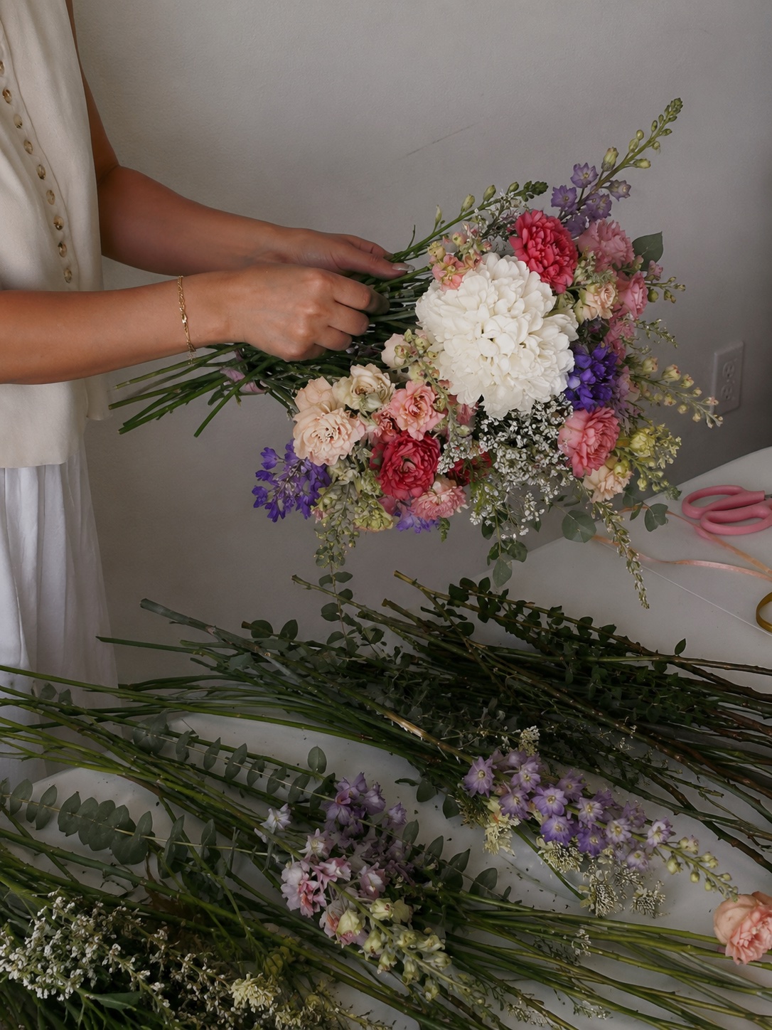 Manos armando un ramo de flores frescas en tonos rosa, blanco y morado